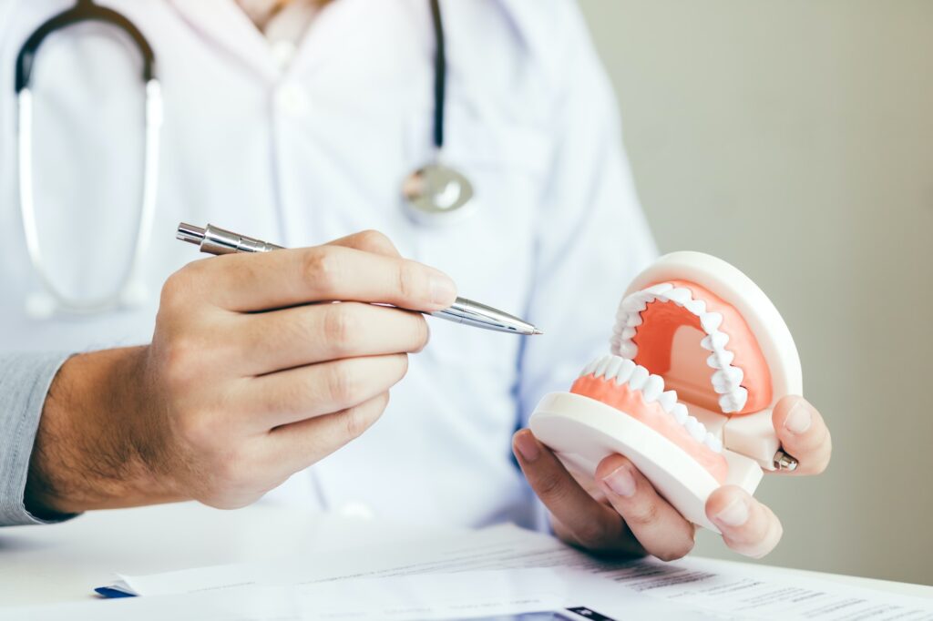 Asian dentist holding pen pointing to the dentures and is describing the problem of teeth.