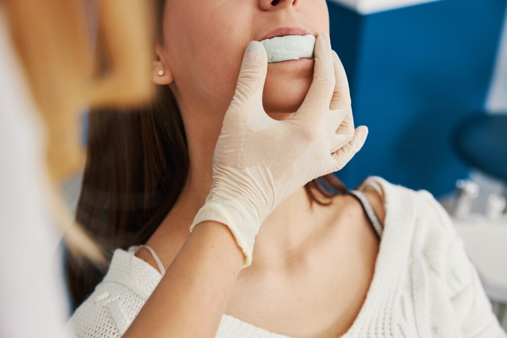 Patient biting on cast mold of jaw, held by dentist